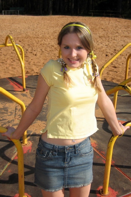 Симпатичная девушка обнажает свой лифчик и трусики под юбкой на детской площадке 1