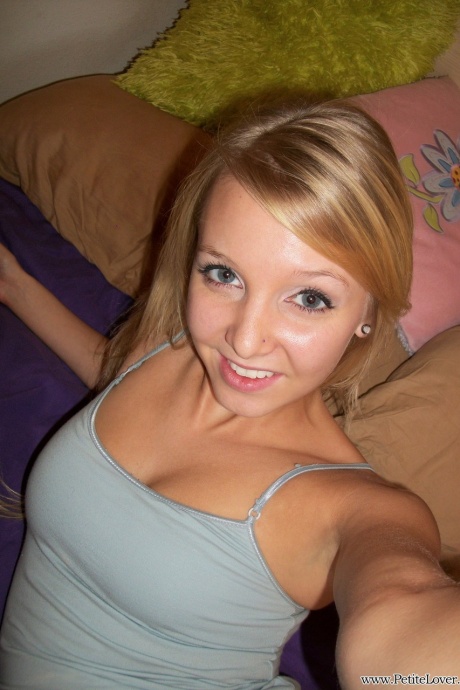 Симпатичная девушка-подросток со светлыми волосами показывает свою безволосую киску на своей кровати 1